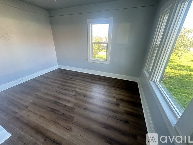 A room with wooden flooring and a window overlooking a green lawn.