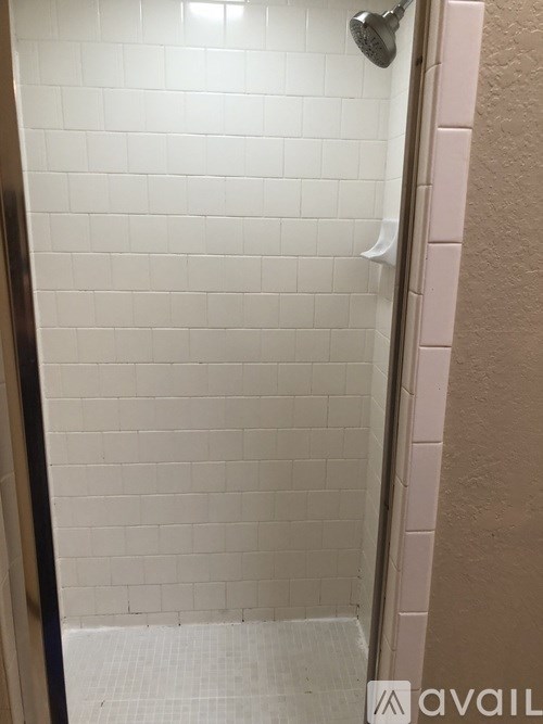 A white tiled shower stall with a door on the left.