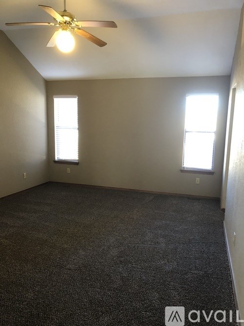 A room with a ceiling fan and two windows.