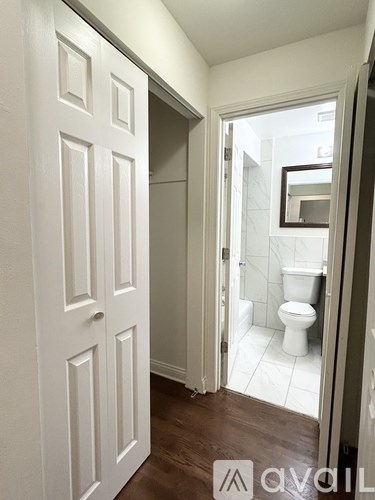 A white door is open to a bathroom with a toilet and a mirror.