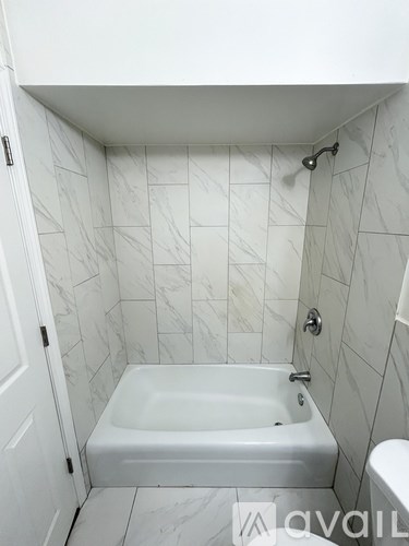 A white bathroom with a marble tile wall and a white bathtub.
