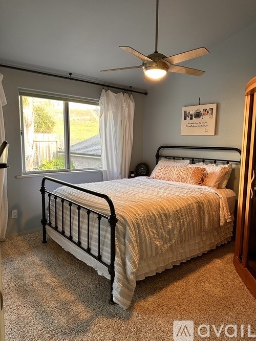 A bedroom with a bed, a ceiling fan, and a window with white curtains.