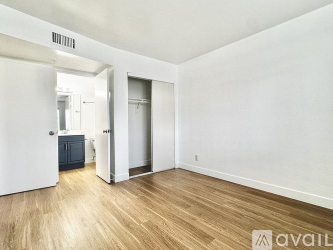 A room with a wooden floor and white walls, with a doorway leading to another room.