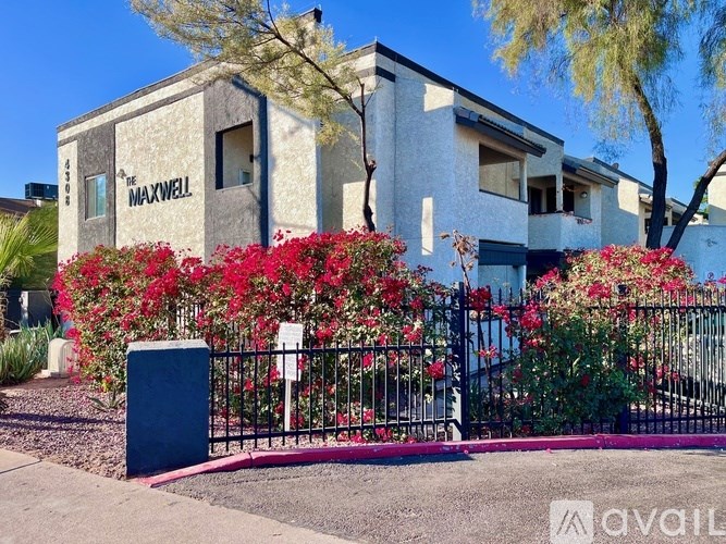 The Maxwell building is surrounded by a black fence and red flowers.
