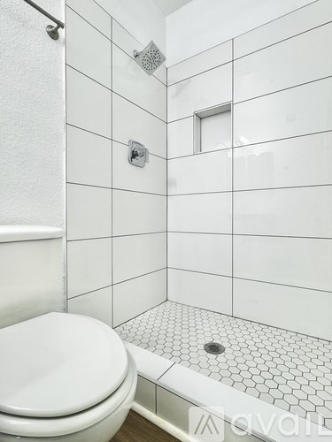 A white toilet in a tiled bathroom with a shower head and a window.