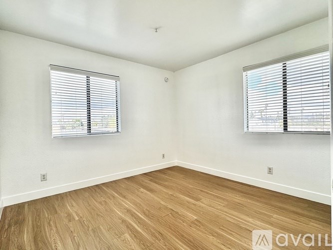A room with wooden flooring and two windows with blinds.