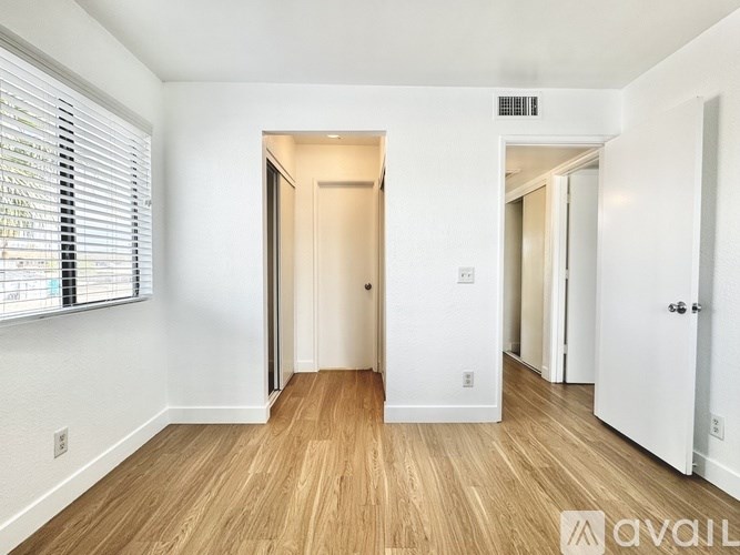 A room with wooden flooring and white walls, with a window on the left side.