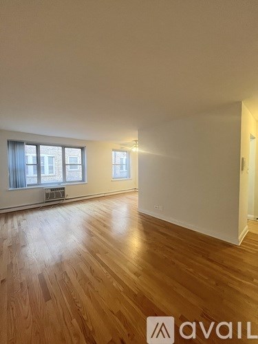 A room with wooden flooring and two windows.