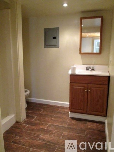A bathroom with a toilet, sink and wooden cabinet.