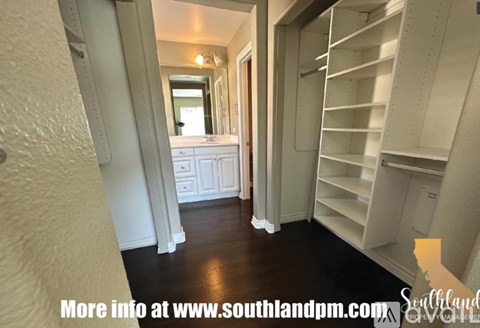 A hallway with a mirror and a door leading to a room with shelves.