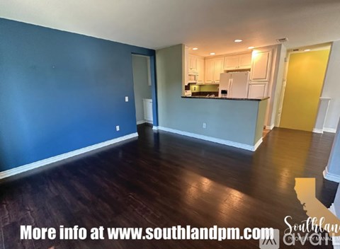 A room with blue walls and wooden flooring, with a kitchen area visible in the background.