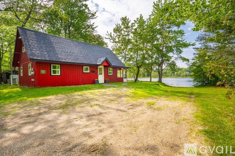 A red barn with a black roof and a dirt driveway in front of it.
