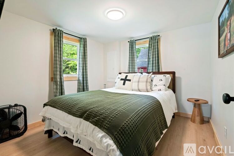 A bedroom with a bed, a fan, and a painting on the wall.