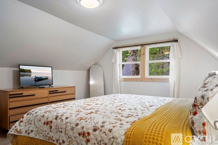 A bedroom with a bed, a dresser with a television on it, and a window with curtains.