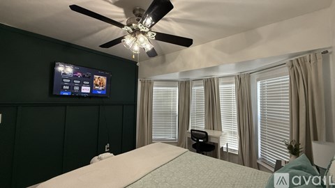 A bedroom with a bed, a ceiling fan, and a television mounted on the wall.