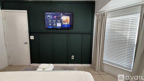 A bedroom with a dark green wall and a flat screen TV mounted on it.