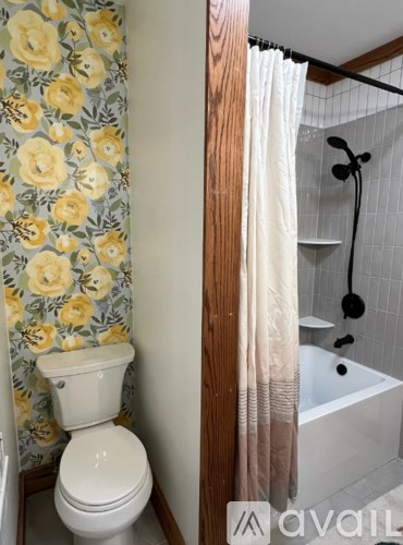 A white toilet with a floral wallpaper next to a white bathtub with a shower curtain.