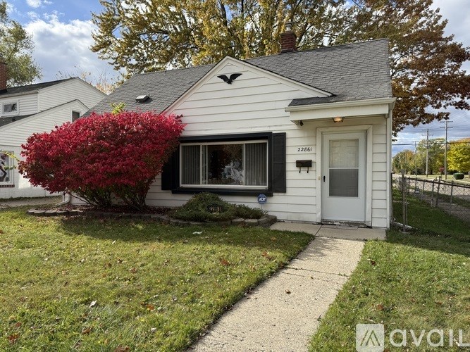 A white house with a red bush in front.
