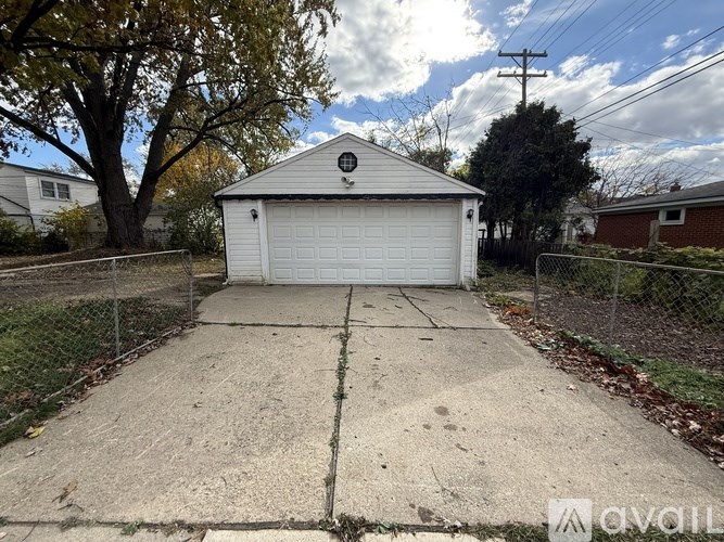 A white garage with a black logo on the front door is surrounded by a chain link fence.