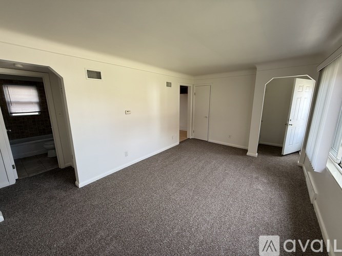 A room with carpeted floor and white walls, with a door and a window.