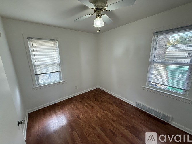 A room with a ceiling fan and two windows.