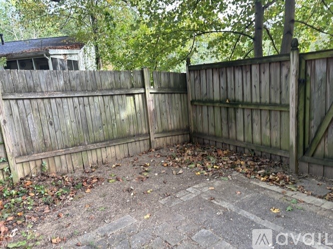 A backyard with a wooden fence and fallen leaves on the ground.