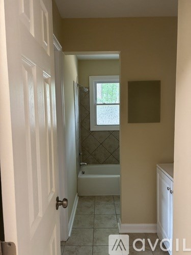 A bathroom with a white door, a window, a tub, and a cabinet.