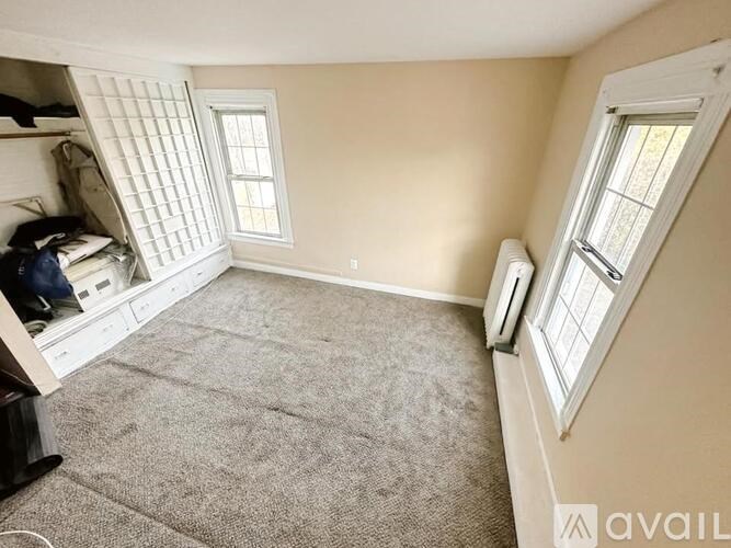A room with a carpeted floor, a window with blinds, and a white door.