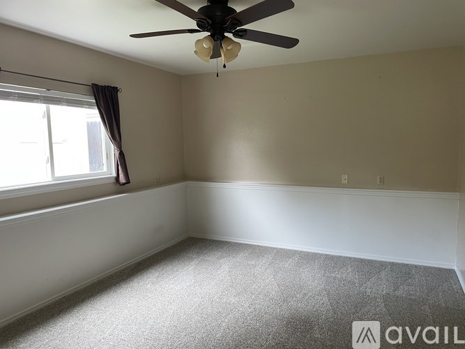 A room with a ceiling fan and a window with curtains.