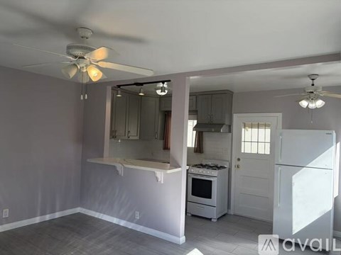 A room with a fan and a kitchen area with a stove and oven.