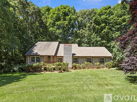 A house with a brown roof and white walls is surrounded by greenery.