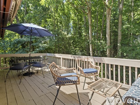 A balcony with chairs and an umbrella overlooking a forest.