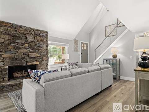 A living room with a grey couch and a stone fireplace.