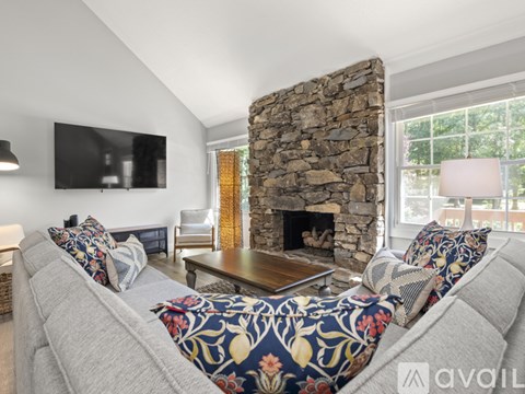 A living room with a grey couch and a stone fireplace.