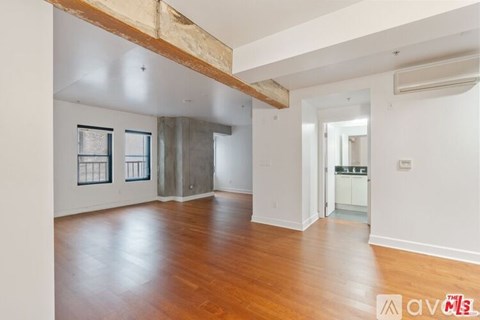 A room with wooden floors and white walls, with a window on the left and a door on the right.
