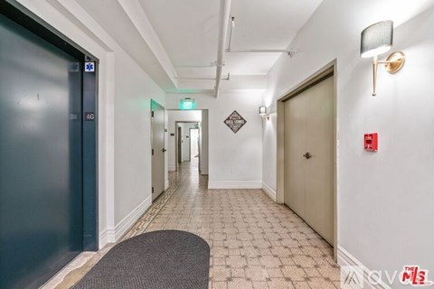 A hallway with a blue door on the left and a red fire alarm on the right.