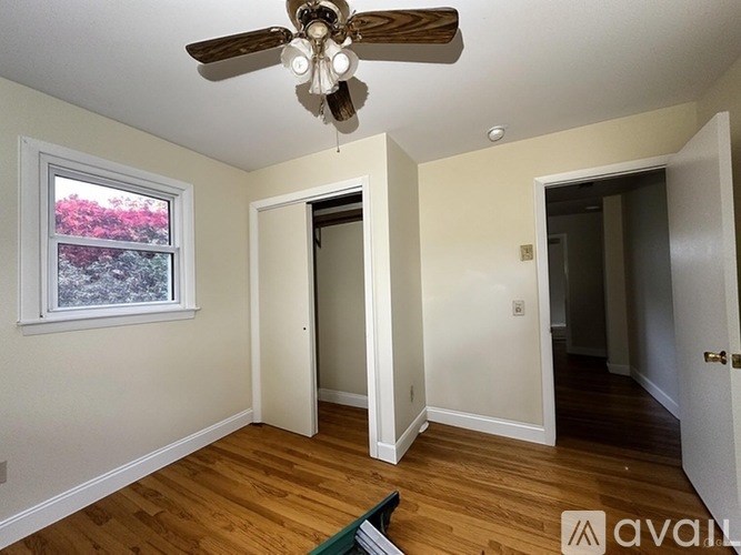 A room with a ceiling fan and a window overlooking a tree-filled landscape.