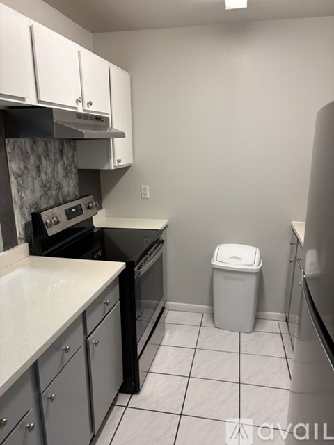 A kitchen with a white counter top and a trash can.