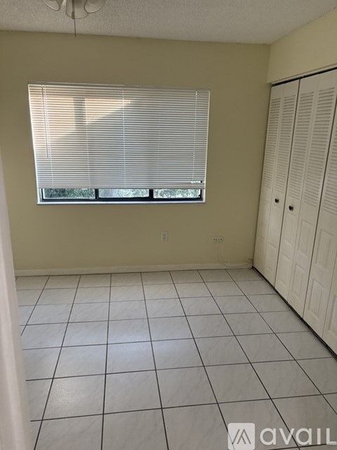 A room with a window covered by white blinds and a white tiled floor.