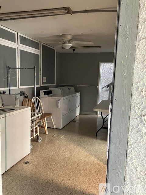 A kitchen with a white fridge, a fan, and a table with chairs.