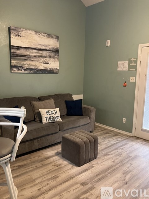 A living room with a couch, chair, ottoman, and a painting on the wall.