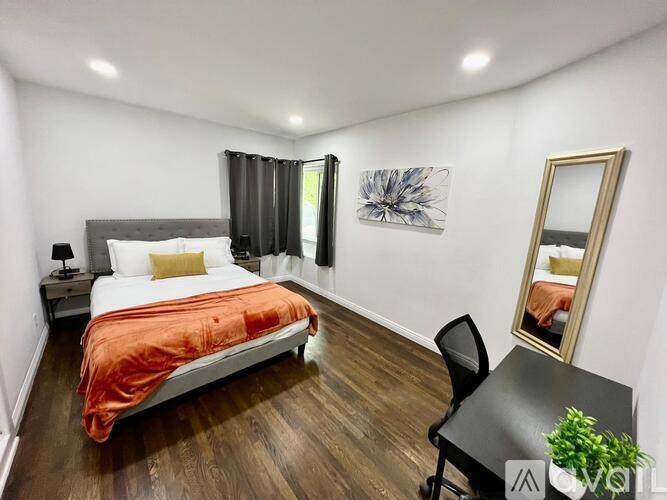 A bedroom with a bed, desk, chair, and a mirror.