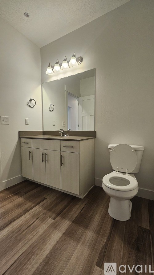 A bathroom with a toilet, a vanity with a mirror and lights above it.