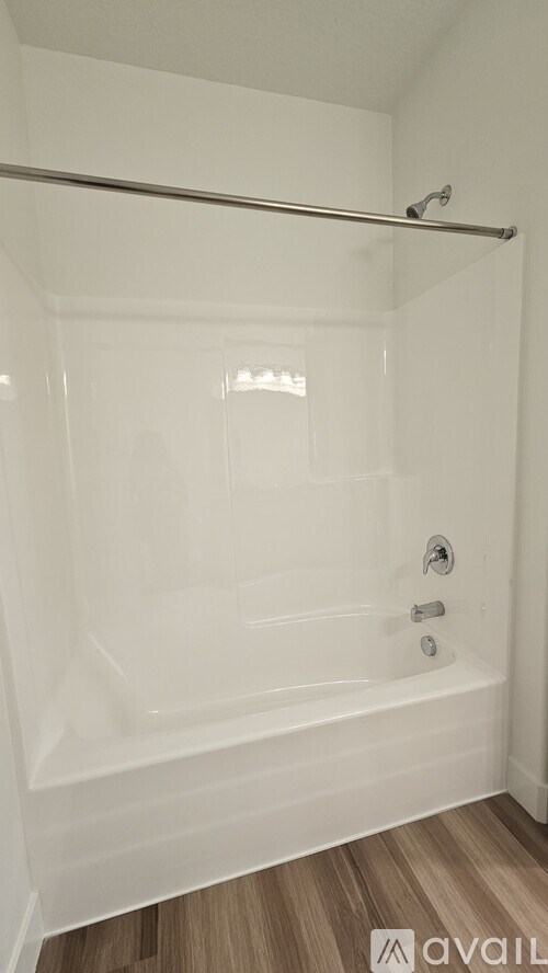 A white bathroom with a glass shower door and a wooden floor.