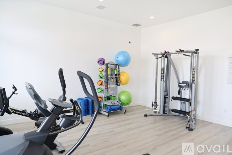 A gym with a variety of equipment including a stationary bike, a rowing machine, and a weight rack.