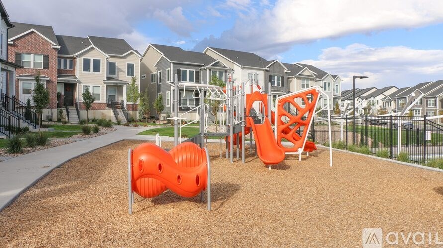 A playground with orange slides and a red climbing frame in front of a row of houses.