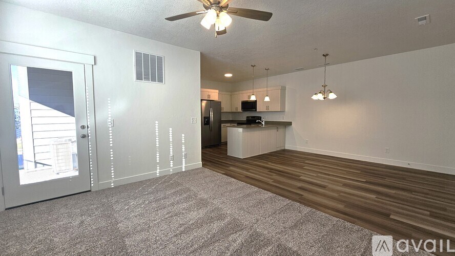 A spacious living room with a ceiling fan and a kitchen area in the background.