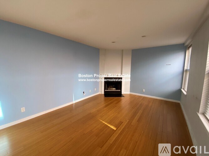 A spacious room with wooden flooring and a fireplace.