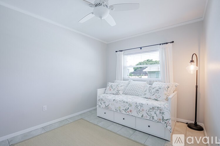A bedroom with a bed, a ceiling fan, and a window with a view of a green landscape.