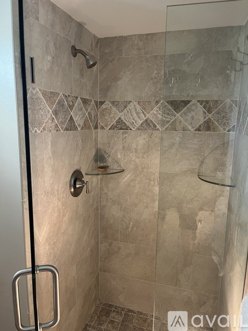 A tiled shower with a glass door and a metal handle.